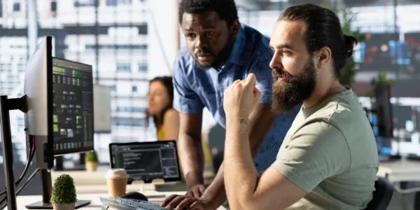 Data engineer and coworker at PC desk developing machine learning algorithms. Programmer and colleague in office solving tasks, training large scale deep learning models using computer