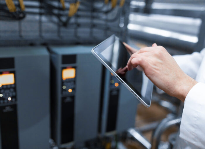 Portrait of man in a white robe and a cap standing in production department of dairy factory with grey tablet technologist with grey tablet in his hands make a set up of the production line while standing at the department of dairy factory