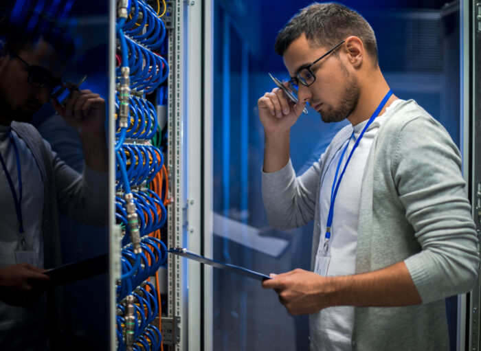 Young Man in Sever Room Side view portrait of young man standing by server cabinet while working with supercomputer in data center and holding clipboard